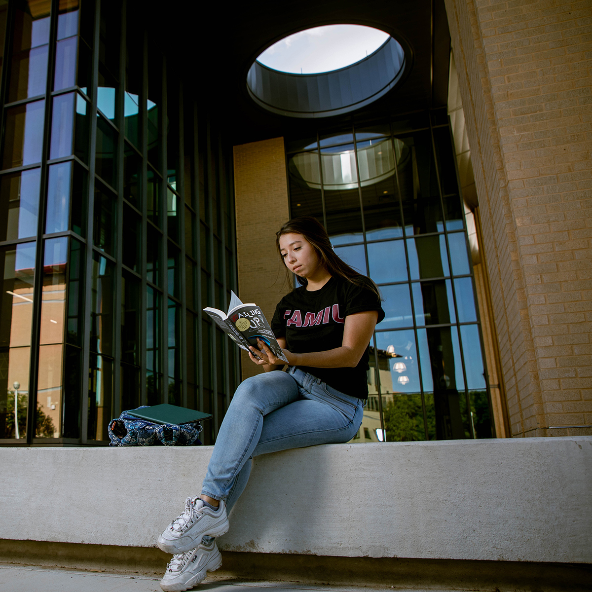 Student reading book on the steps of TAMIU's Academic Innovation Center building