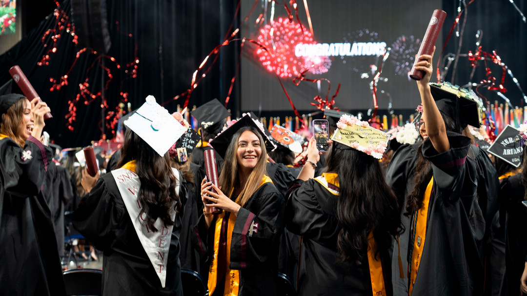 A graduate smiles brightly as streamers cascade onto the floor of the Sames Auto Arena.